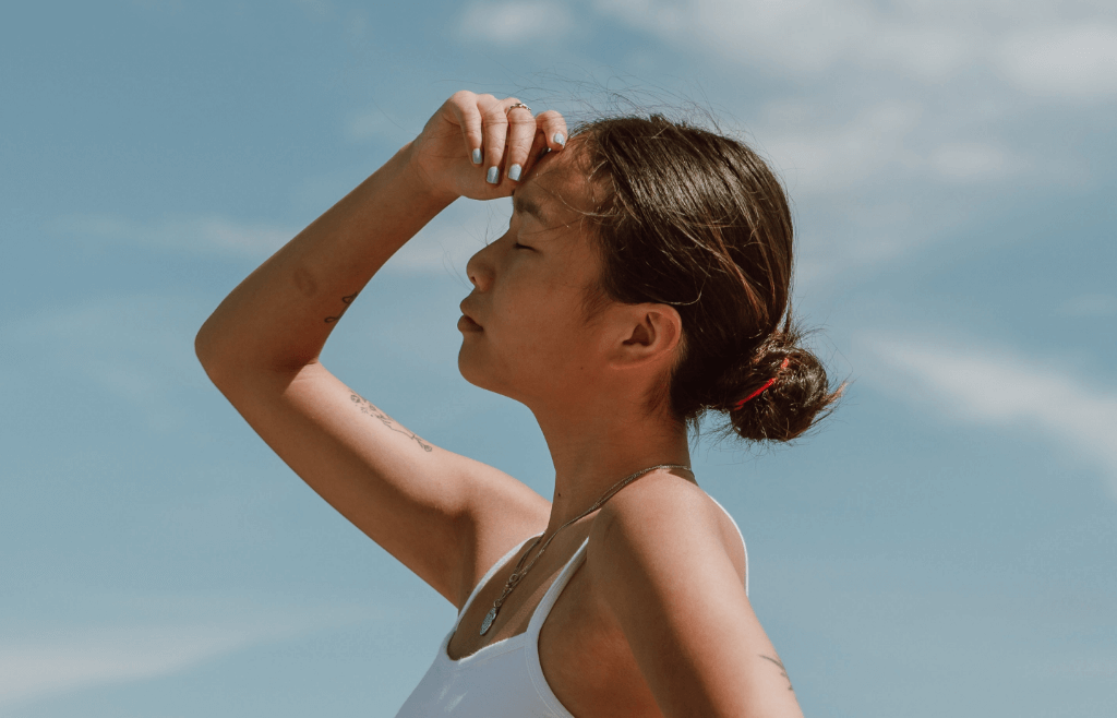 Brown haired girl looking up at the sun blocking her eye with her hand.