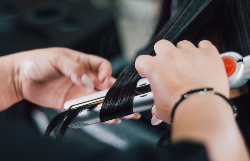 A person using a hair straightener on straight, black hair.