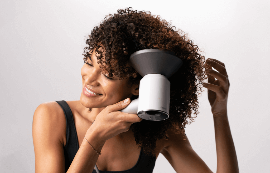 a woman with very coiled hair defusing her curls with a dyson blow dryer