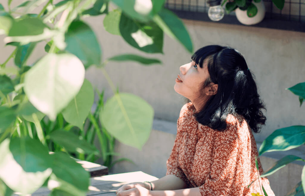 an asian woman sitting in the shade wearing a burnt orange blouse with a white pattern on it