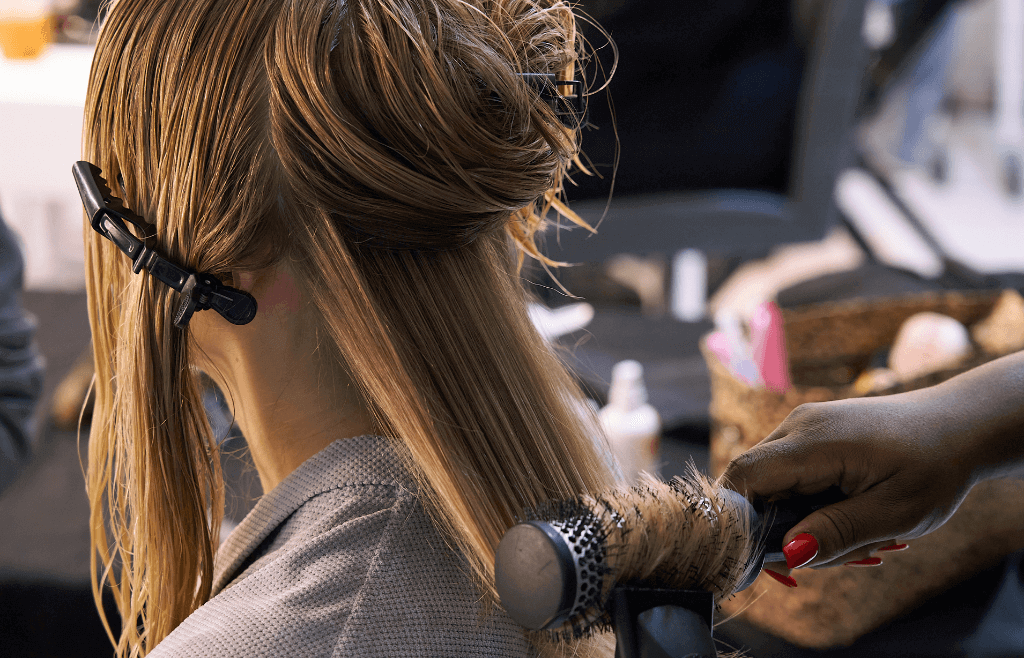 a woman at the hair dressers getting her hair styled using a blow dryer and round brush