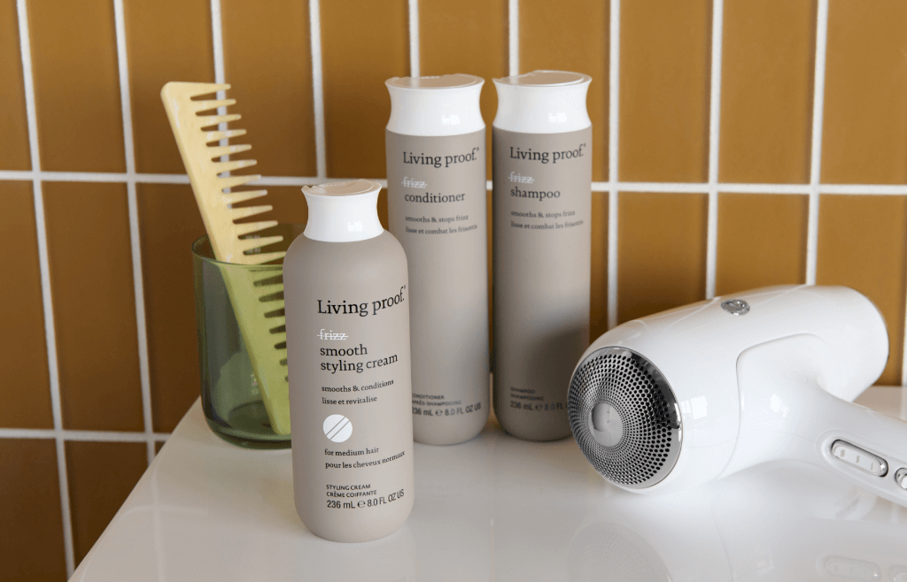Bottles of Living Proof frizz products on a counter with a hair dryer and a comb