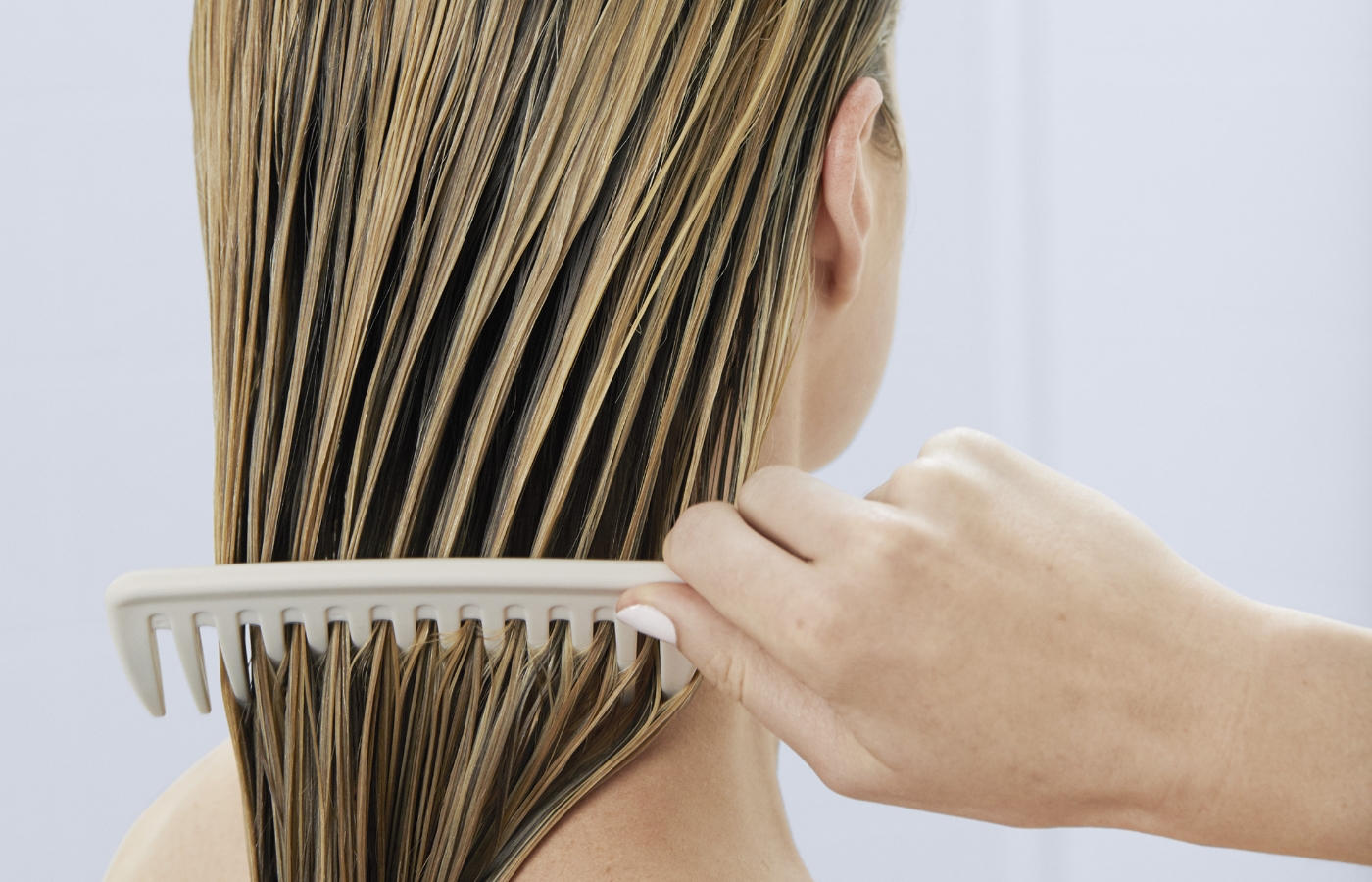 Woman brushing wet hair with wide-tooth comb.