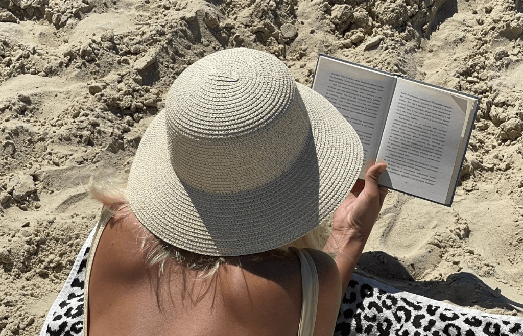 Woman lying on the beach reading a book wearing a sunhat