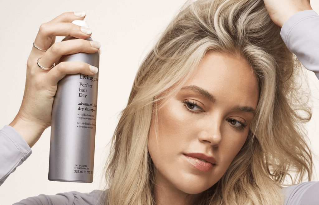 Image of a woman with mid-length blonde hair applying dry shampoo.