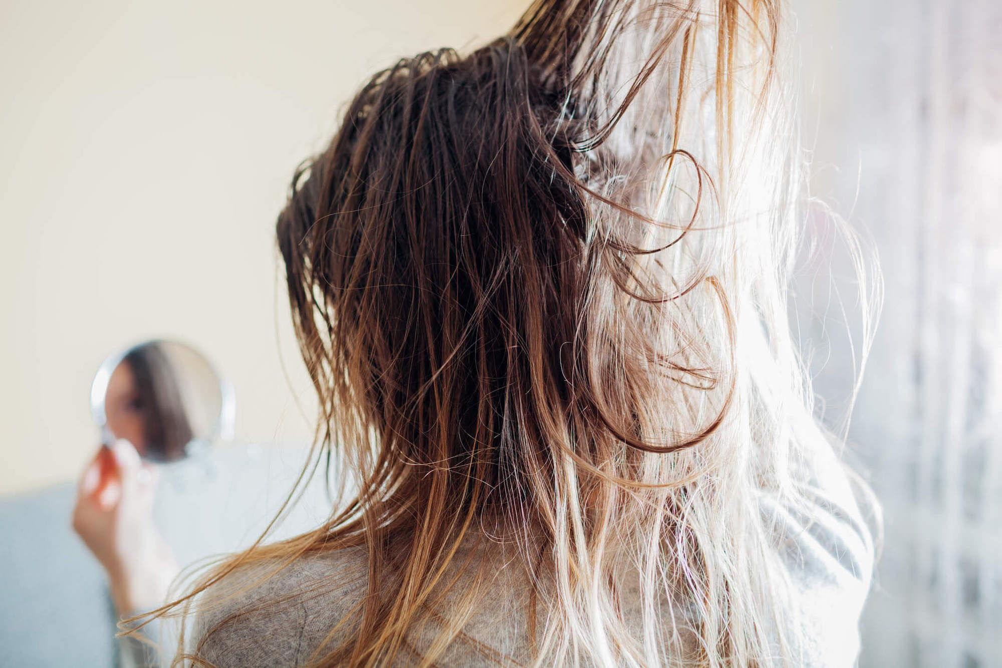 Person examining their hair with visible residue, highlighting the consequences of silicone in hair products.